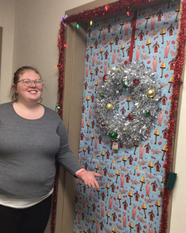 smiling woman showing front door of her apartment, covered in Christmas decorations