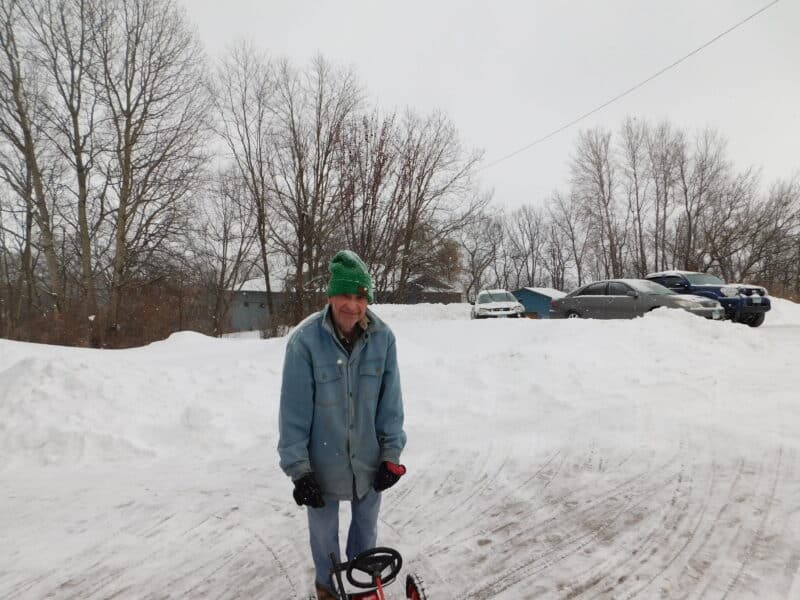 man in jacket and green hat standing on plowed driveway in winter