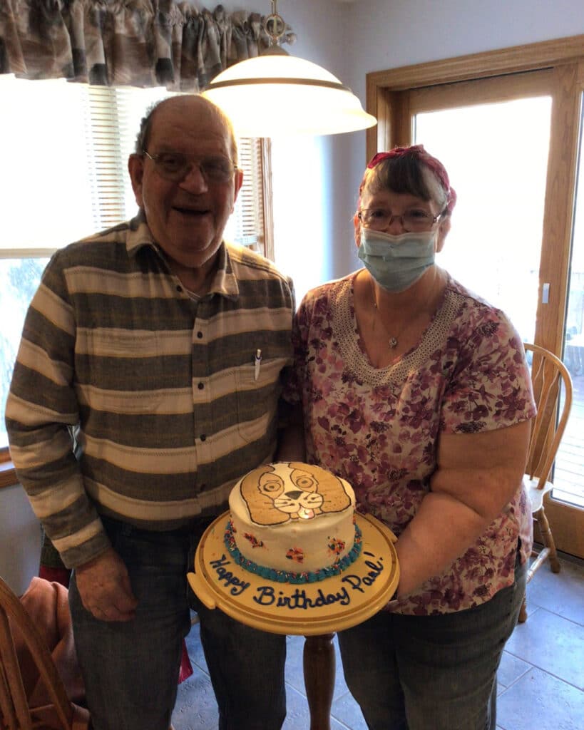 smiling man and woman holding cake with decoration of a dog and text Happy birthday