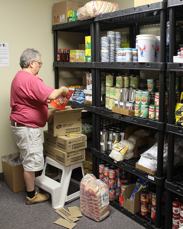 person unpacking a box in front of shelves full of canned and dry food supplies